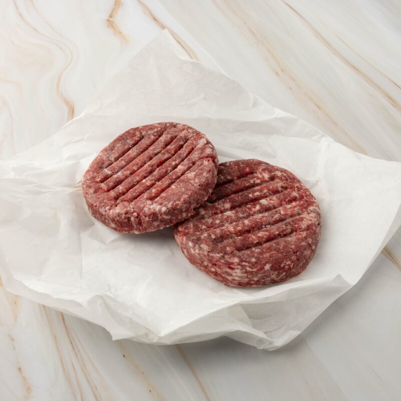 Zwei rohe Hamburger-Patties auf Papier.