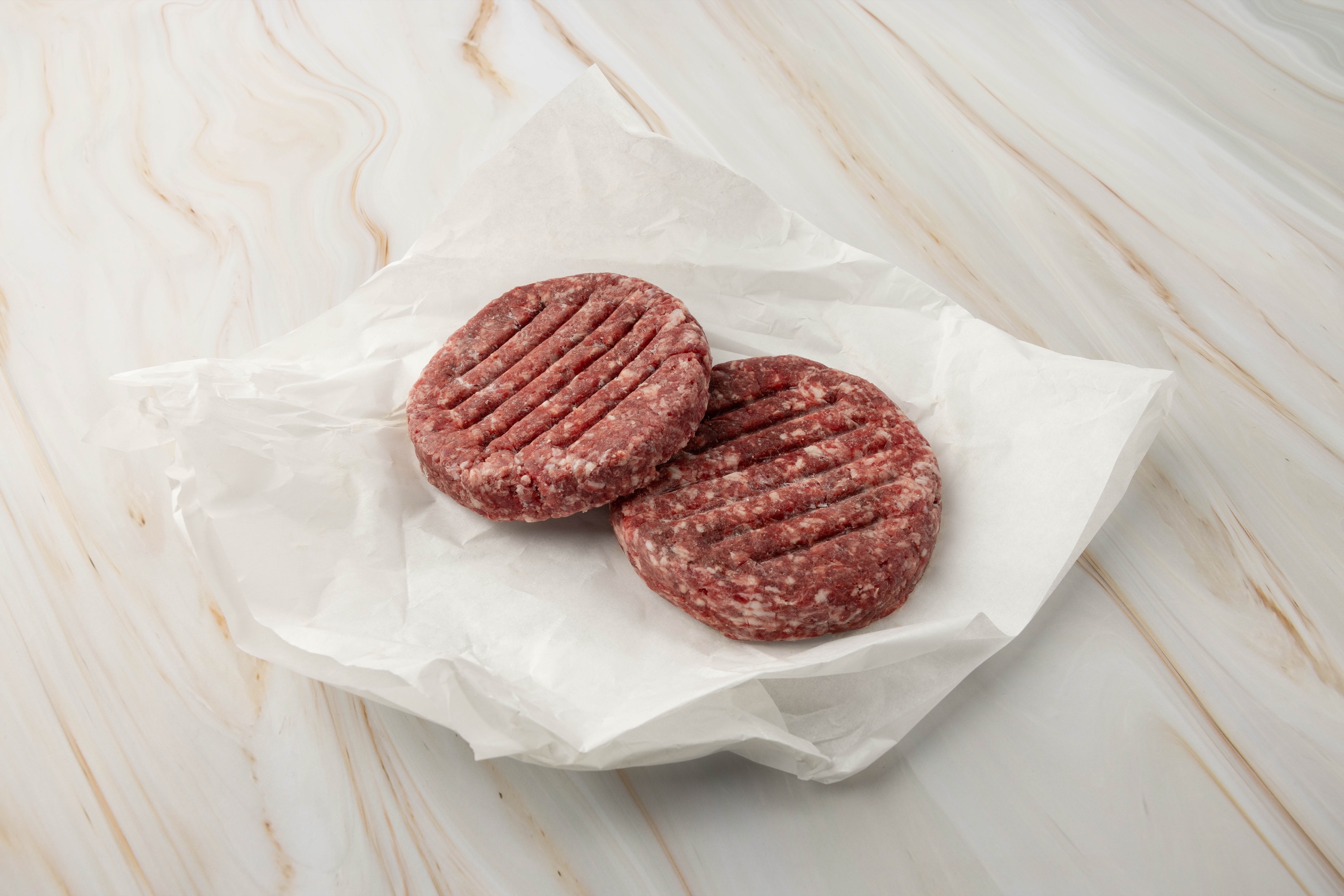 Zwei rohe Hamburger-Patties auf Papier.